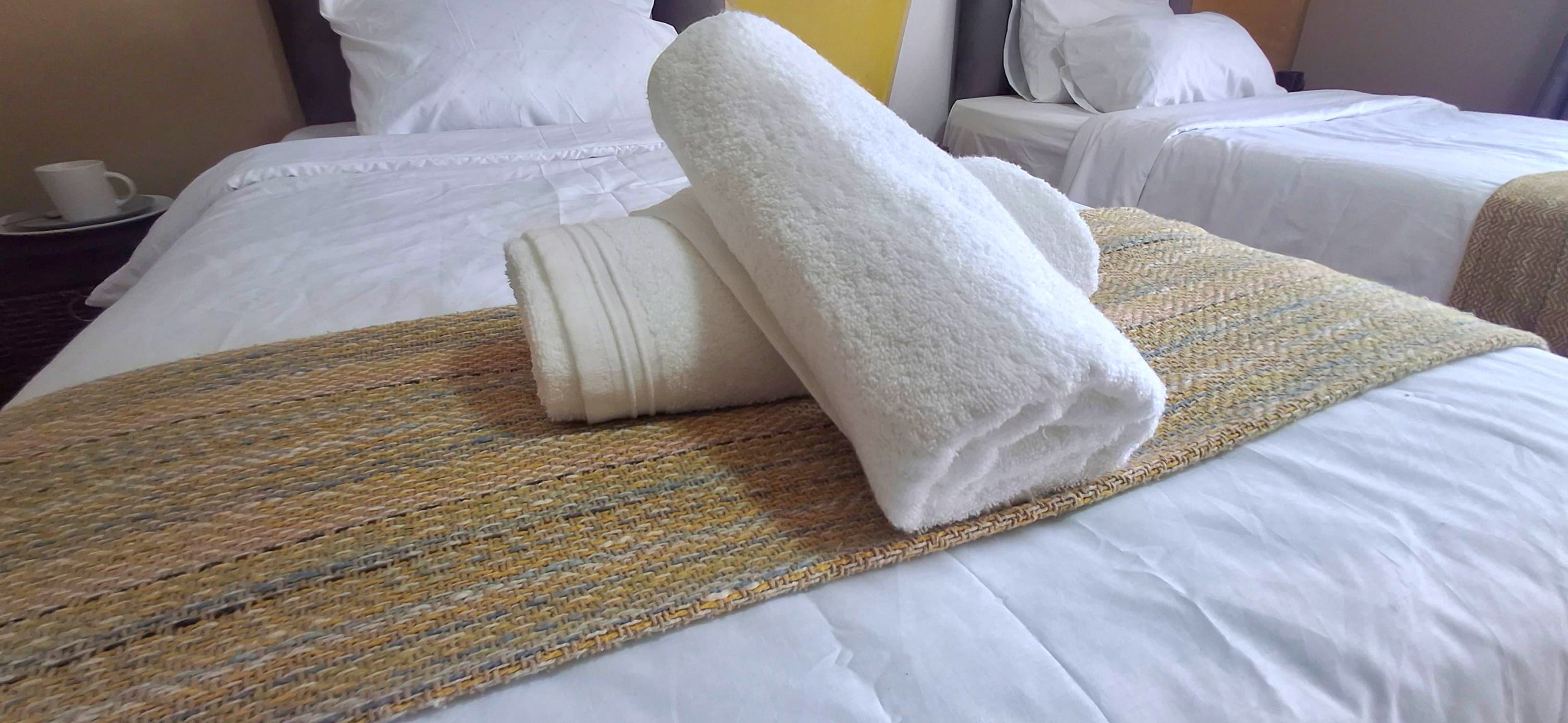 Twin beds dressed with white linen, runners, and rolled towels